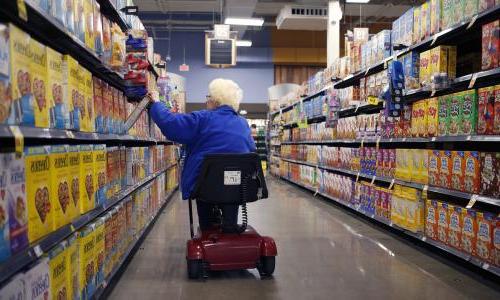 An older woman in a scooter goes down the cereal aisle of a supermarket