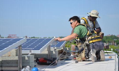 Two workers install solar panels on a roof